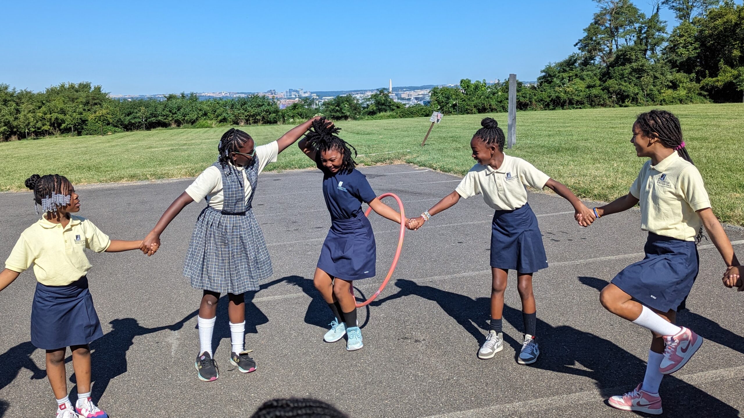 Students are in a line holding hands, passing a hula hoop through the line.