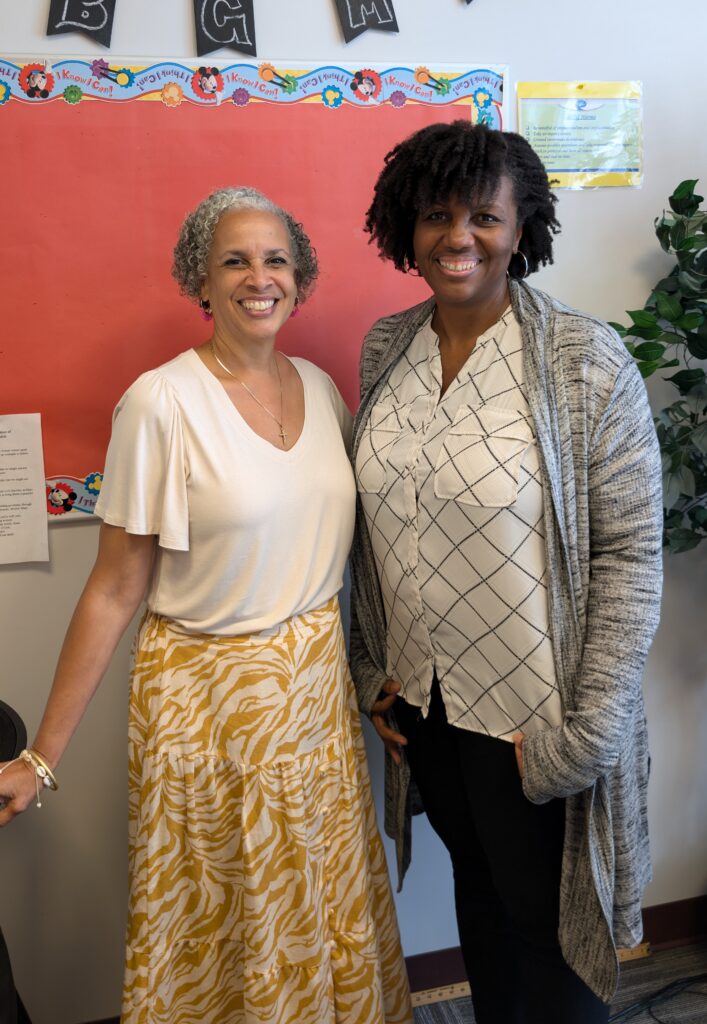 Two black women stand together, smiling towards the camera.