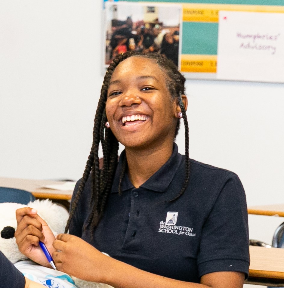 A Black teenaged girl smiles in her classroom